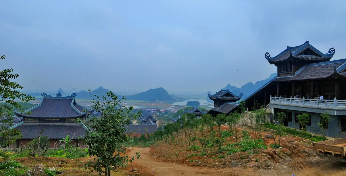 Temple roofs on a hillside under a cloudy sky with distant hills