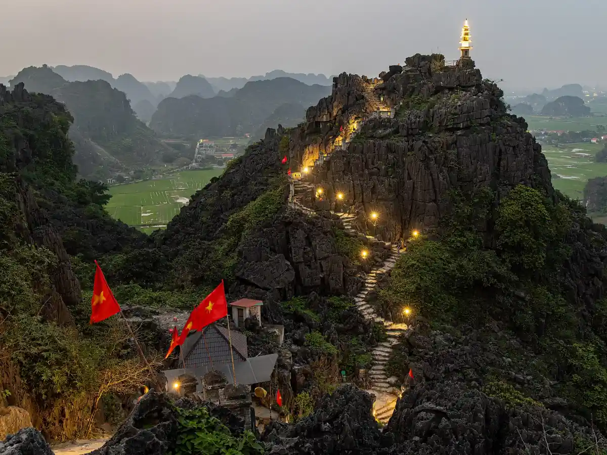 Lit stairway climbing a karst peak topped by a pagoda at dusk