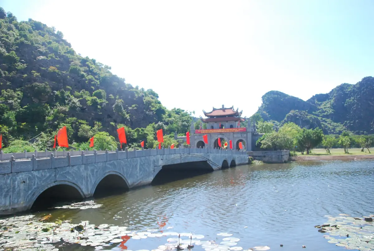 Stone bridge over a pond leading to a red gate with karst behind