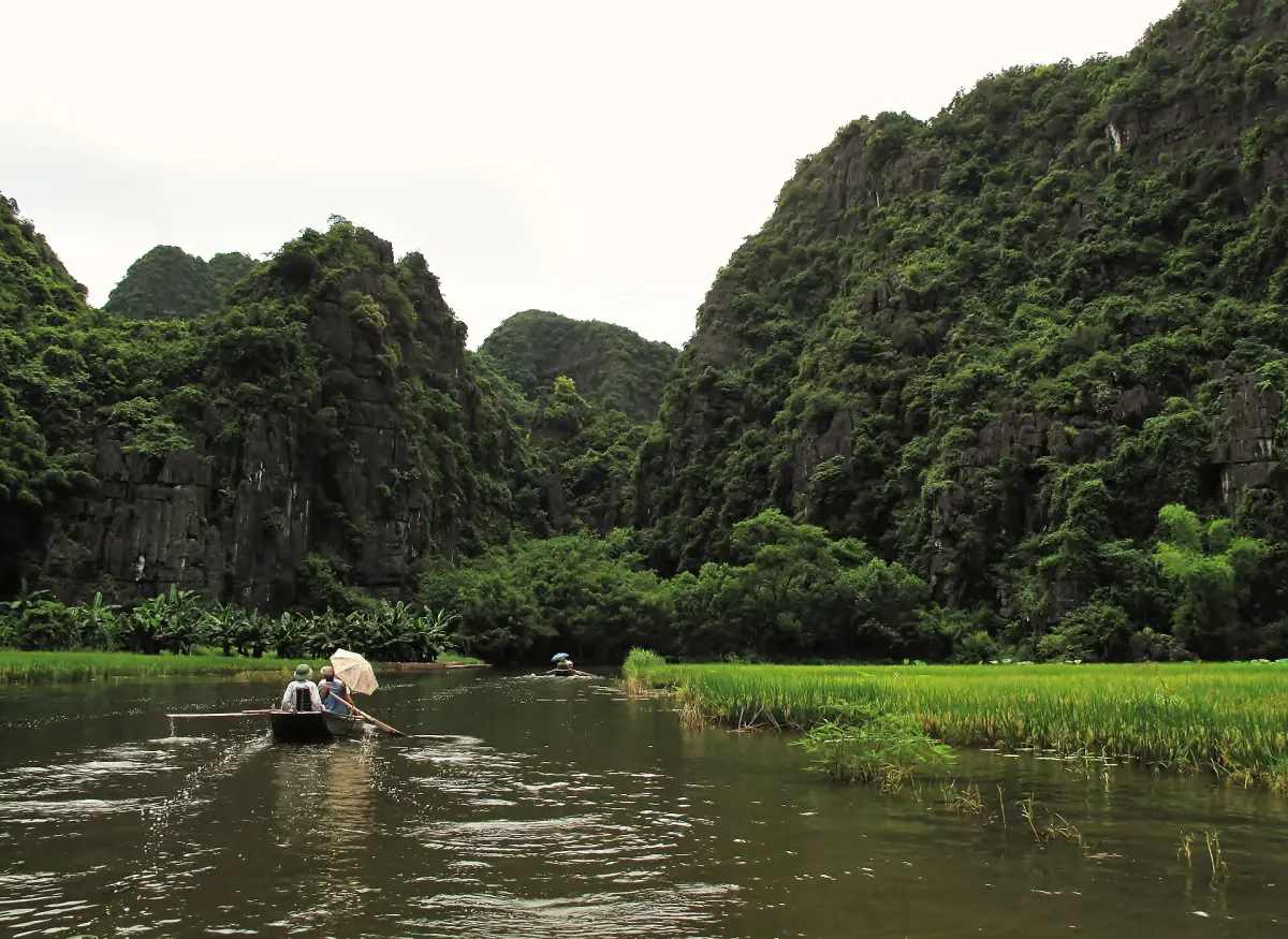 Small boat on a quiet river between green limestone cliffs