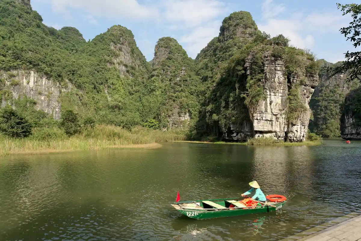 Rower in a small boat on calm green water between limestone karst