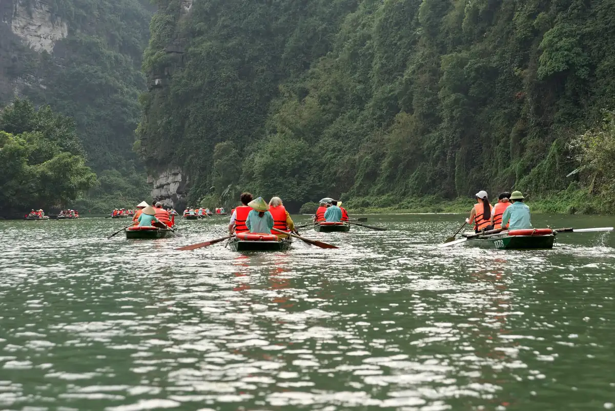 Rowing boats carrying visitors along a river beneath forested limestone cliffs