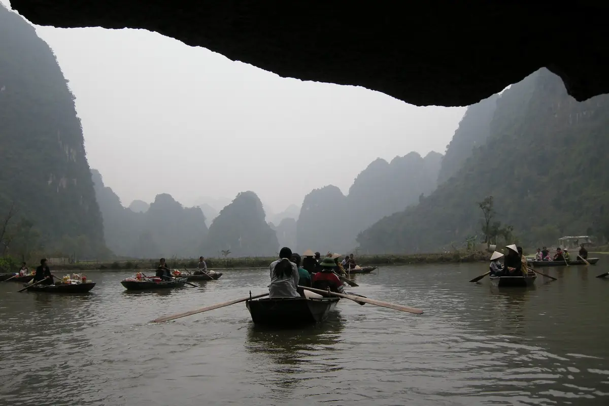 Boats passing through a cave opening toward misty karst valley