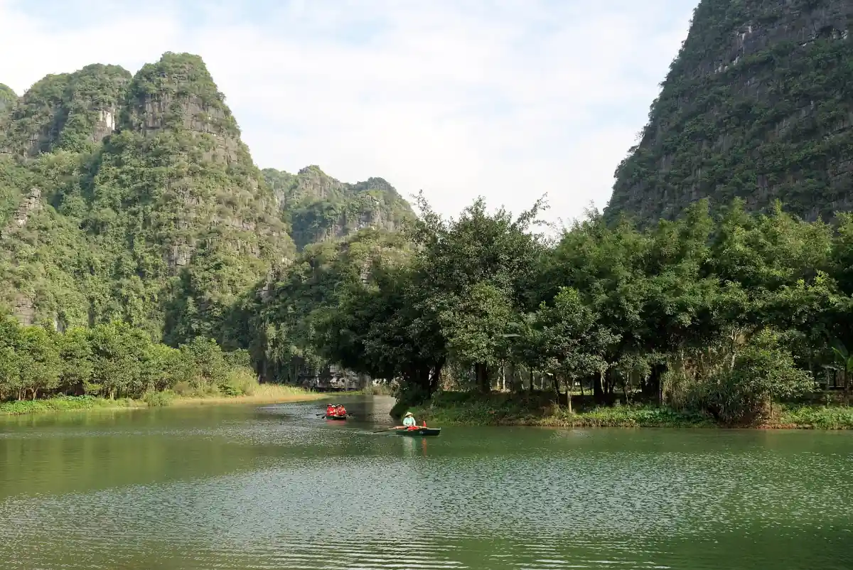 Calm lake with trees and tall limestone peaks under a bright sky